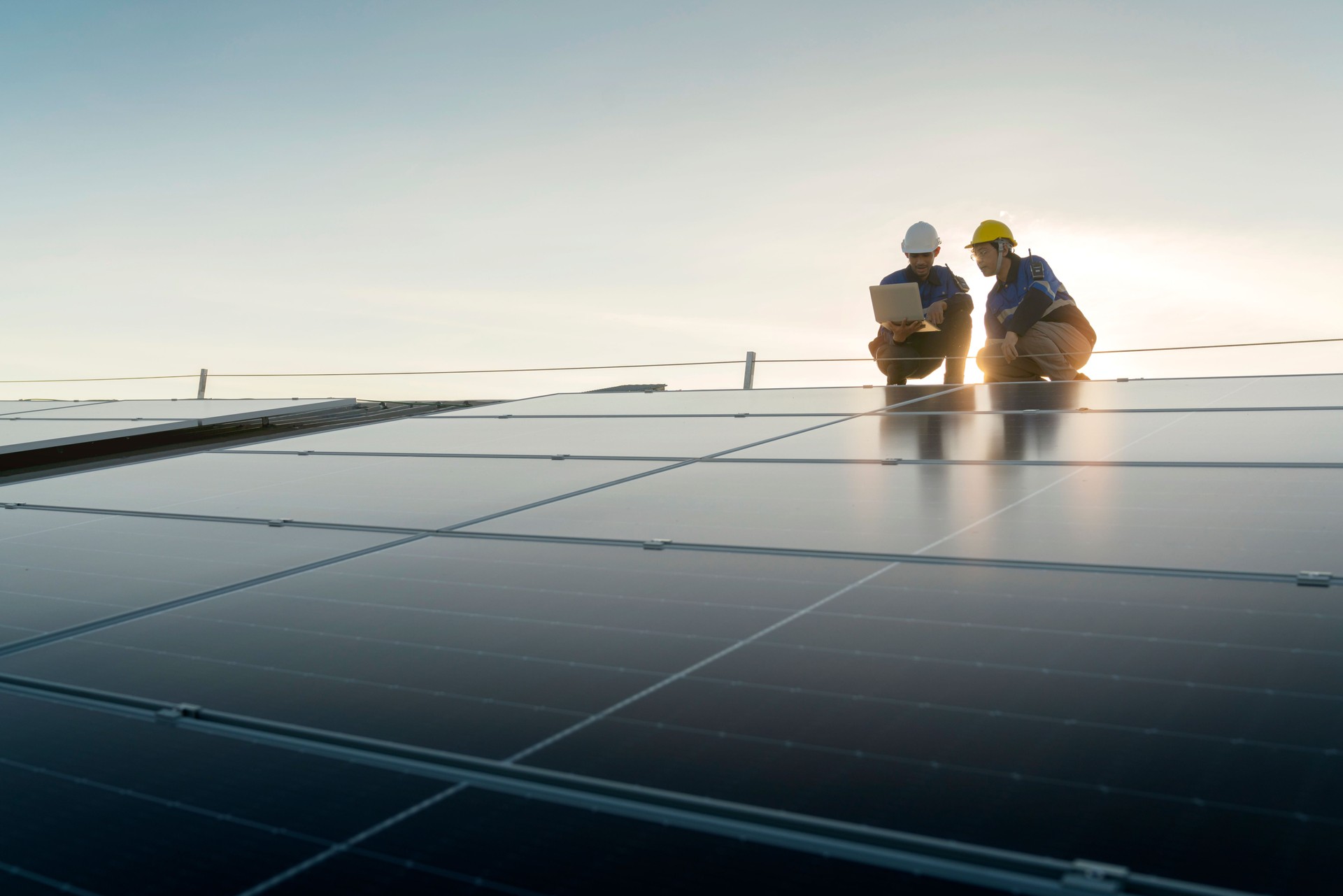 Técnico especialista ingeniero profesional con control de mantenimiento de computadoras portátiles y tabletas instalando paneles solares en el techo de la fábrica bajo la luz solar. La encuesta del equipo de ingenieros verifica el techo del panel solar.